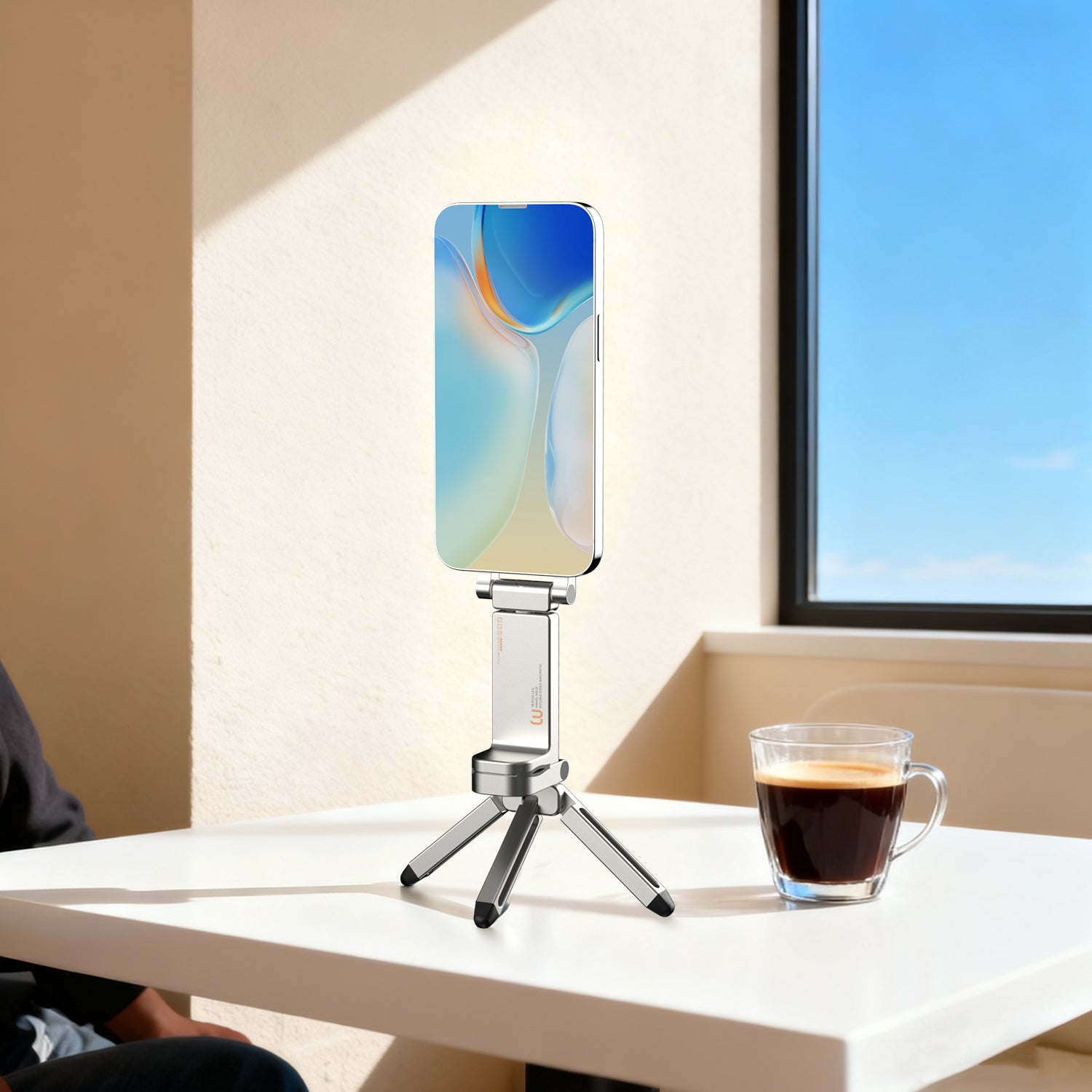 Compact MagSafe travel tripod standing on a table beside a coffee cup.